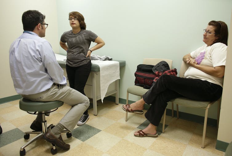A doctor speaking with a young transgender person and their mother.