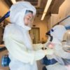 Two scientists in a COVID-19 research laboratory, wearing fully enclosed white protective suits with clear face screens and independent air supplies.