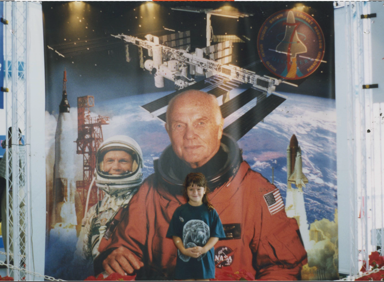 smiling girl stands in front of a John Glenn space mural
