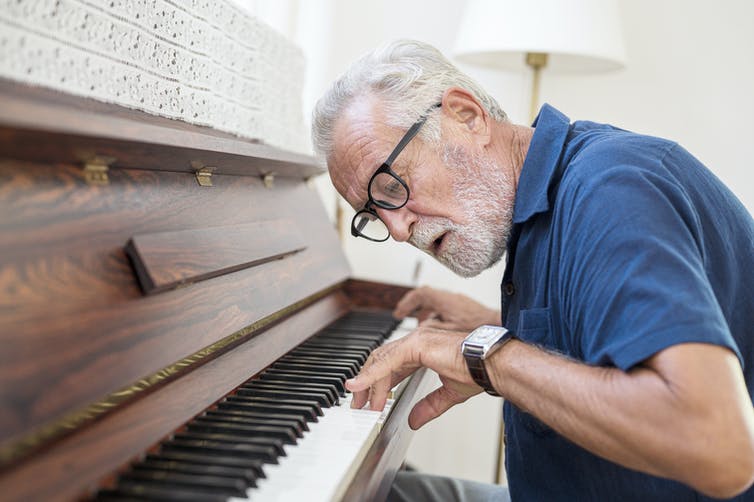 older man leans in and looks at his hands on the piano keyboard