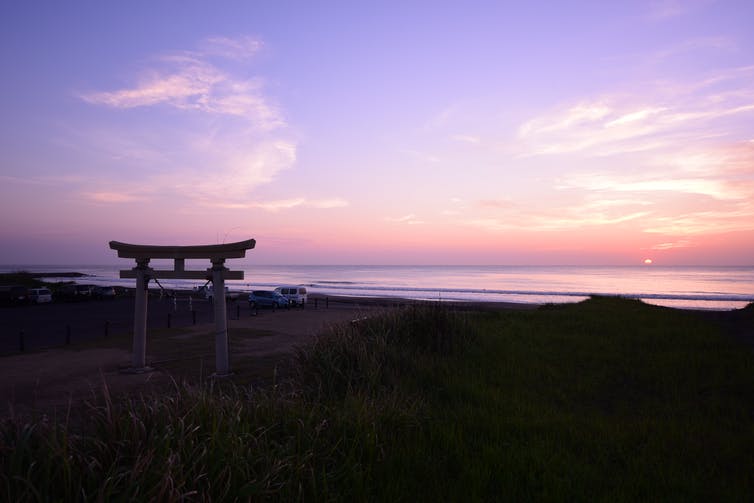 A sunrise over a beach with a Japanese arch in the foreground.