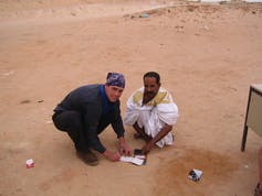 Two people kneeling in the sand over a piece of paper.