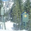 A small green metal tower and green wooden box in a snowy mountain forest.