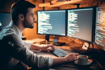 Focused developer coding on computer monitors working late in office