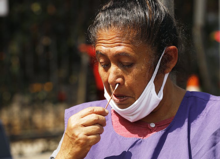 woman with lowered mask swabs her own nose