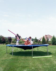 A family on a trampoline with the trampoline stretching down toward the ground.