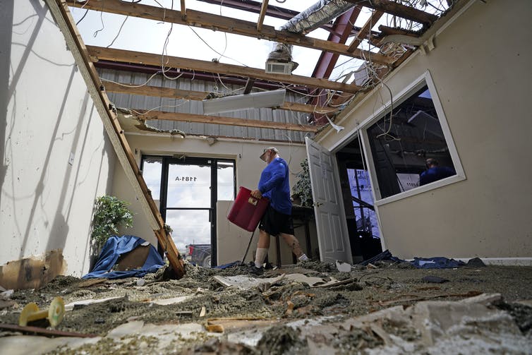 A man walks through the debris of an office with the roof torn off.