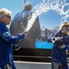 Richard Branson in a blue jumpsuit celebrated his successful sub-orbital flight to space by spraying champagne on a stage.