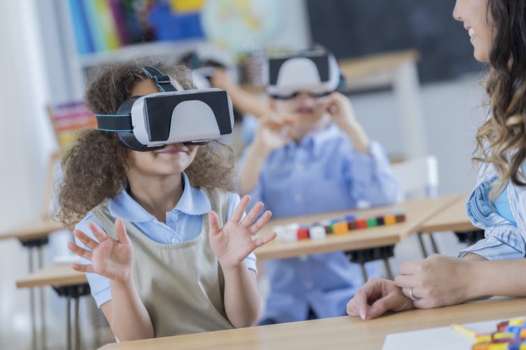 A group of young girls wear VR headsets in class.