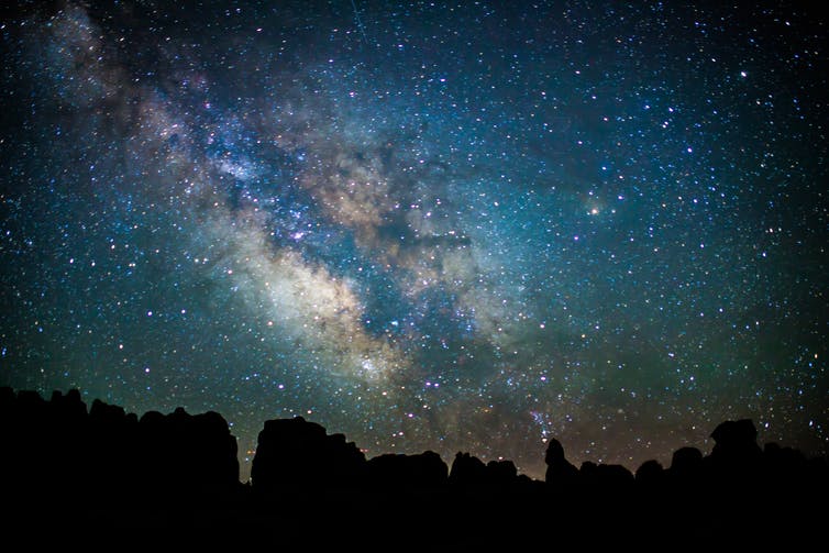 A nighttime photograph taken at Utah's Canyonlands National Park, looking skyward and revealing thousands of stars in the Milky Way.