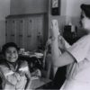 Smiling boy rolls up his sleeve to get a shot from a nurse