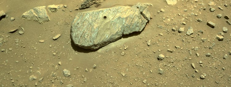 A rock on reddish brown surface with a circular hole drilled into the top.