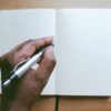 hand with pen poised above empty notebook pages