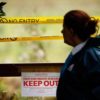 A woman stands in front of an area cordoned off with caution tape and a sign saying 'Keep Out.'