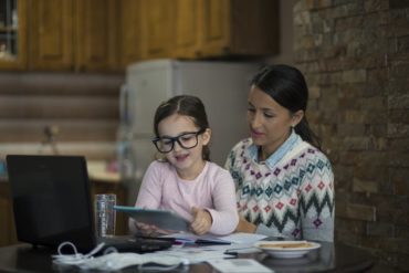 A mother and her young daughter together looking at the computer screen.