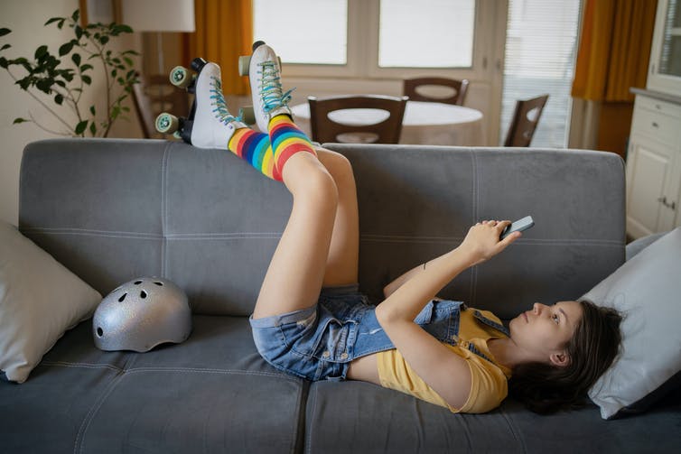 Person lying down with rainbow sock-clad legs resting on the back of a sofa.