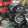 The crumpled front end of a wrecked car against the rear end of a fire engine