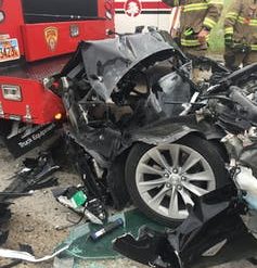 The crumpled front end of a wrecked car against the rear end of a fire engine