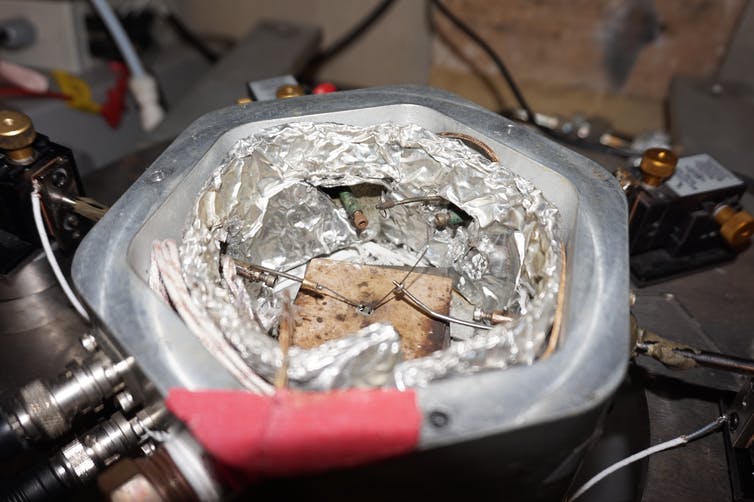 A small square of material inside a test chamber of metal with tubes.