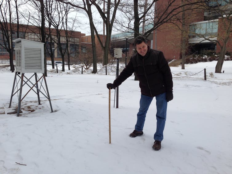 man leans on ruler poking into snow-covered ground