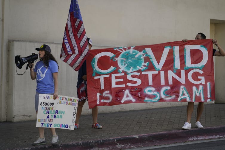 a woman speaks into a bullhorn while two people hold a banner behind her