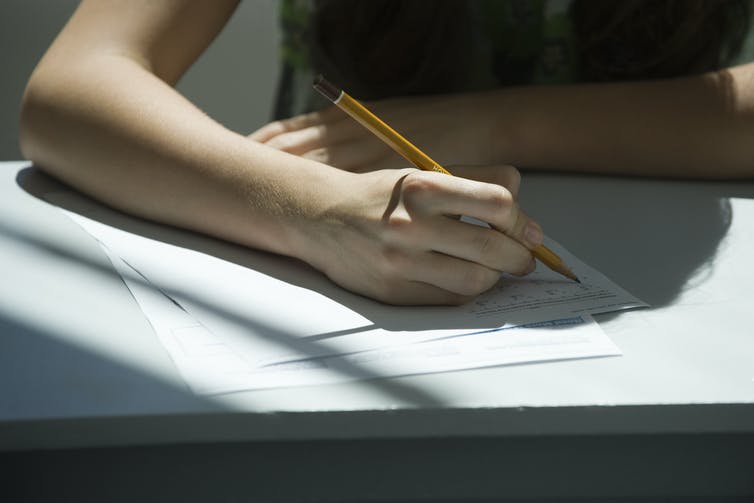 A person holding a pencil above a sheet of paper.
