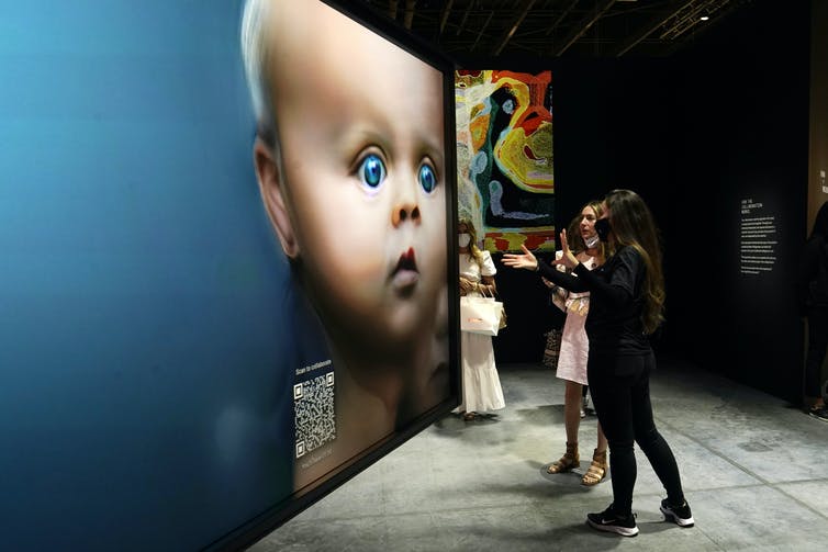 Three women stand in a room with angled walls covered with images