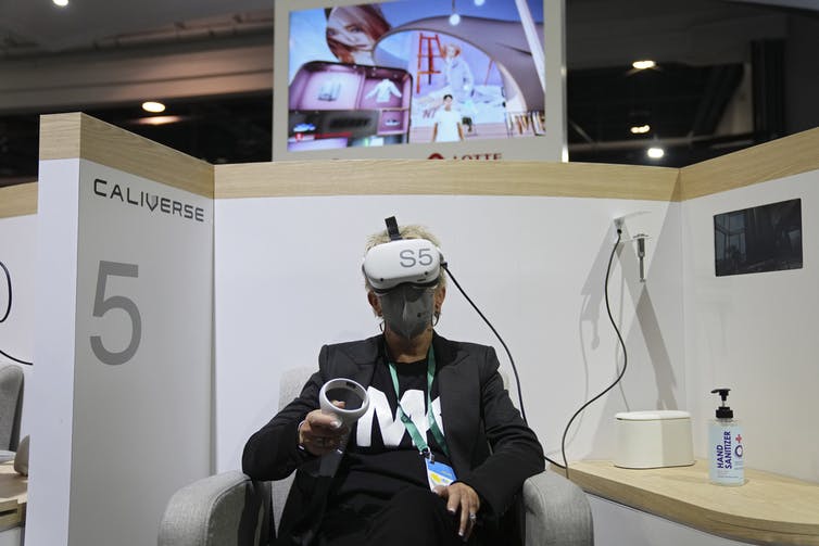 A woman wearing virtual reality goggles sits in a trade show booth