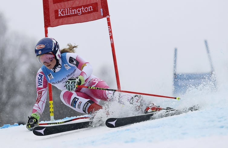 A woman making a tight turn on skis around a red gate.