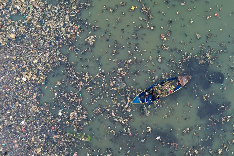 Aerial shot of boat floating through plastic pollution on water