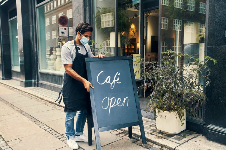 masked cafe worker puts out an 'open' sign