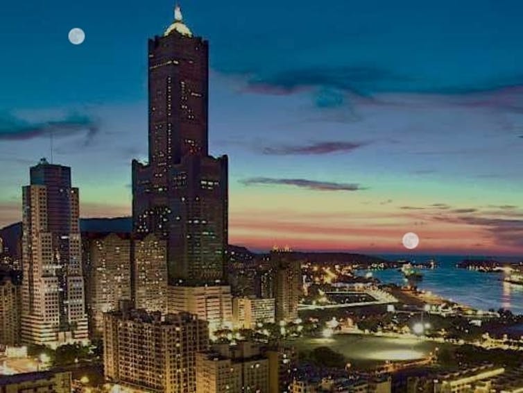 An image of a city skyline with two images of the Moon – one higher in the sky and one near a distant horizon.