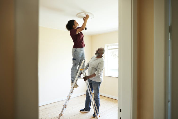 man holds ladder while woman works on ceiling fixture
