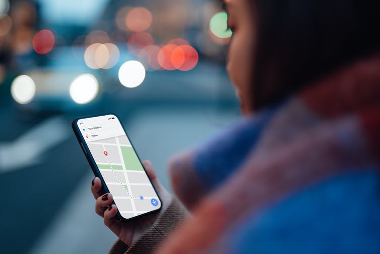 over-the-shoulder view of a young woman on a city street holding a smart phone displaying a map