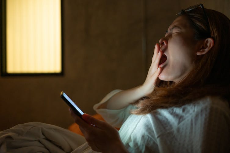 yawning woman holding a glowing phone