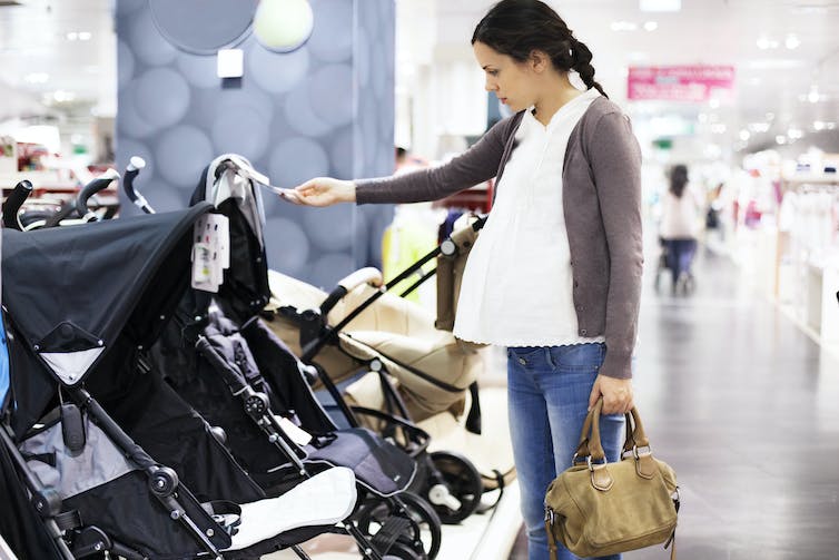 pregnant woman looks at strollers in a store