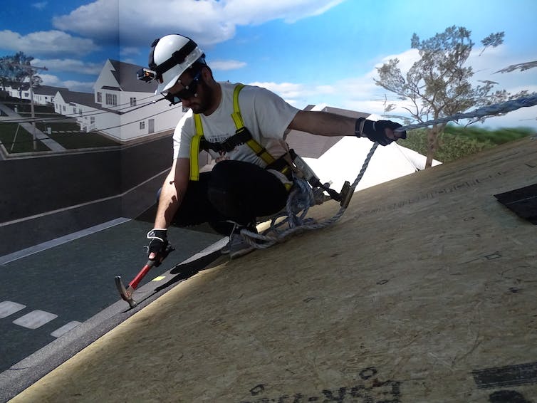 man roped in with safety equipment uses a hammer on a sloped surface with virtual background