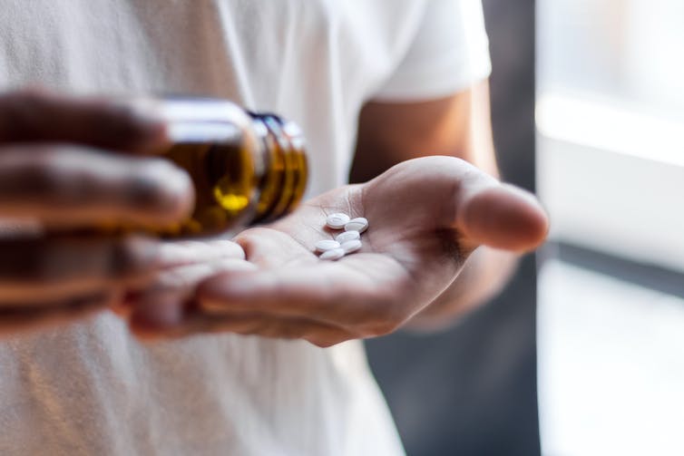 Person dispensing white pills from a bottle into hand.