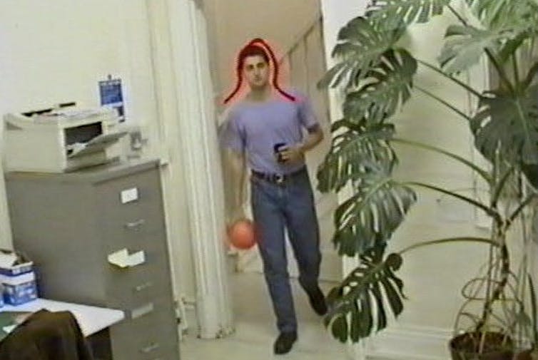 a color video frame showing a young man entering a room with a red curve overlaying the image outlining his head