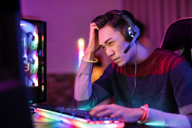Man with gaming headphones looks distressed while staring at his screen.