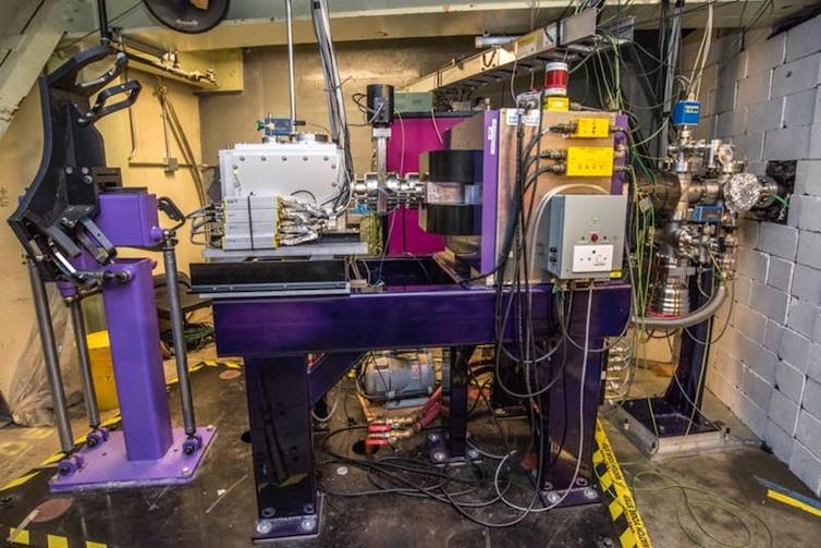 A purple piece of machinery in a concrete room with metal boxes and cables coming off it.