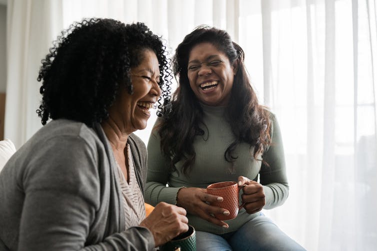 two seated women laughing with mugs in their hands