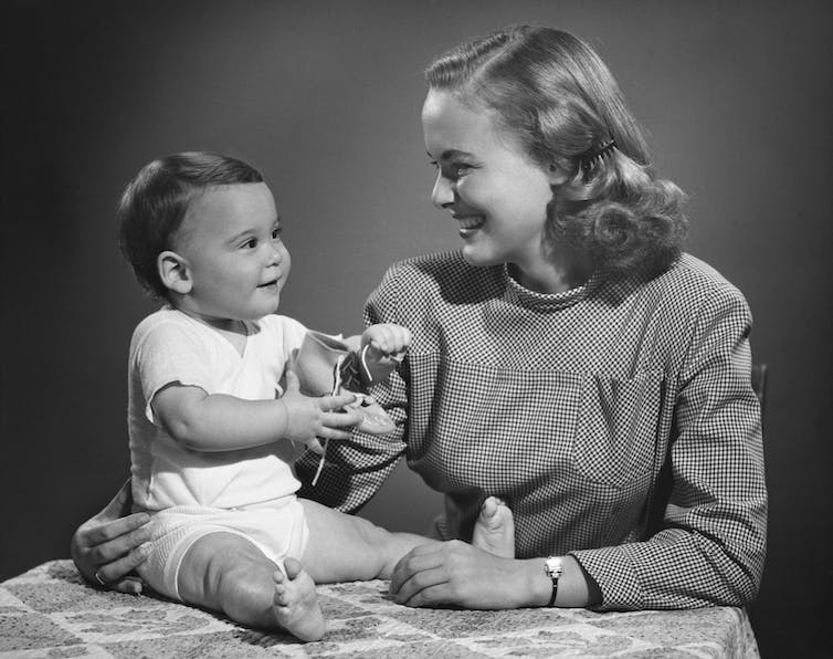 Black and white 1950s photo of a seated baby with a smiling woman