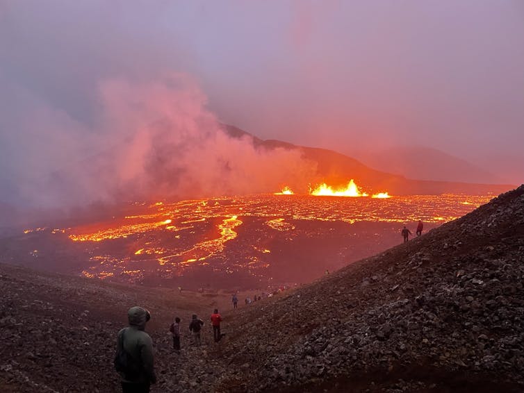 A group of people watch a lava-covered mountin from afar