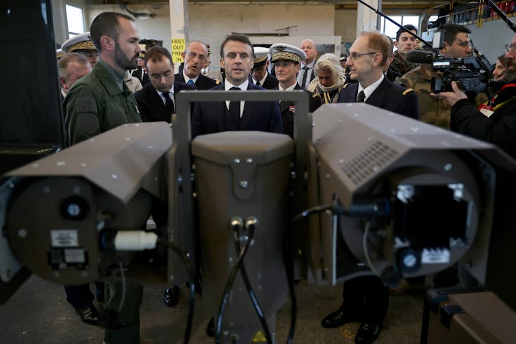 A pair of horizontal metal cylinders in the foreground and a group of people business suits and military uniforms in the background