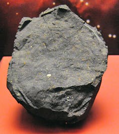 A large grey rock with flecks of orange and green position on a display table.