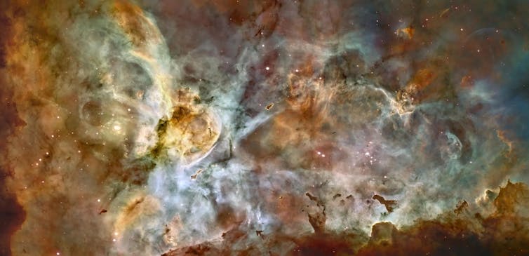 In space, orange, blue and black clouds swirl together with stars visible through the haze.