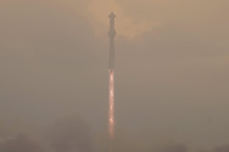 A long, cylindrical rocket lifts off through fog.