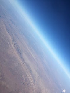 A photo of Earth's atmosphere, with a bright white horizon line that fades into space.