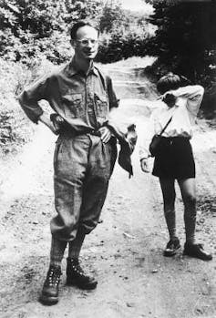 André Weil, aged about 50, stands on a sunny path. A child is standing next to him shielding their face.